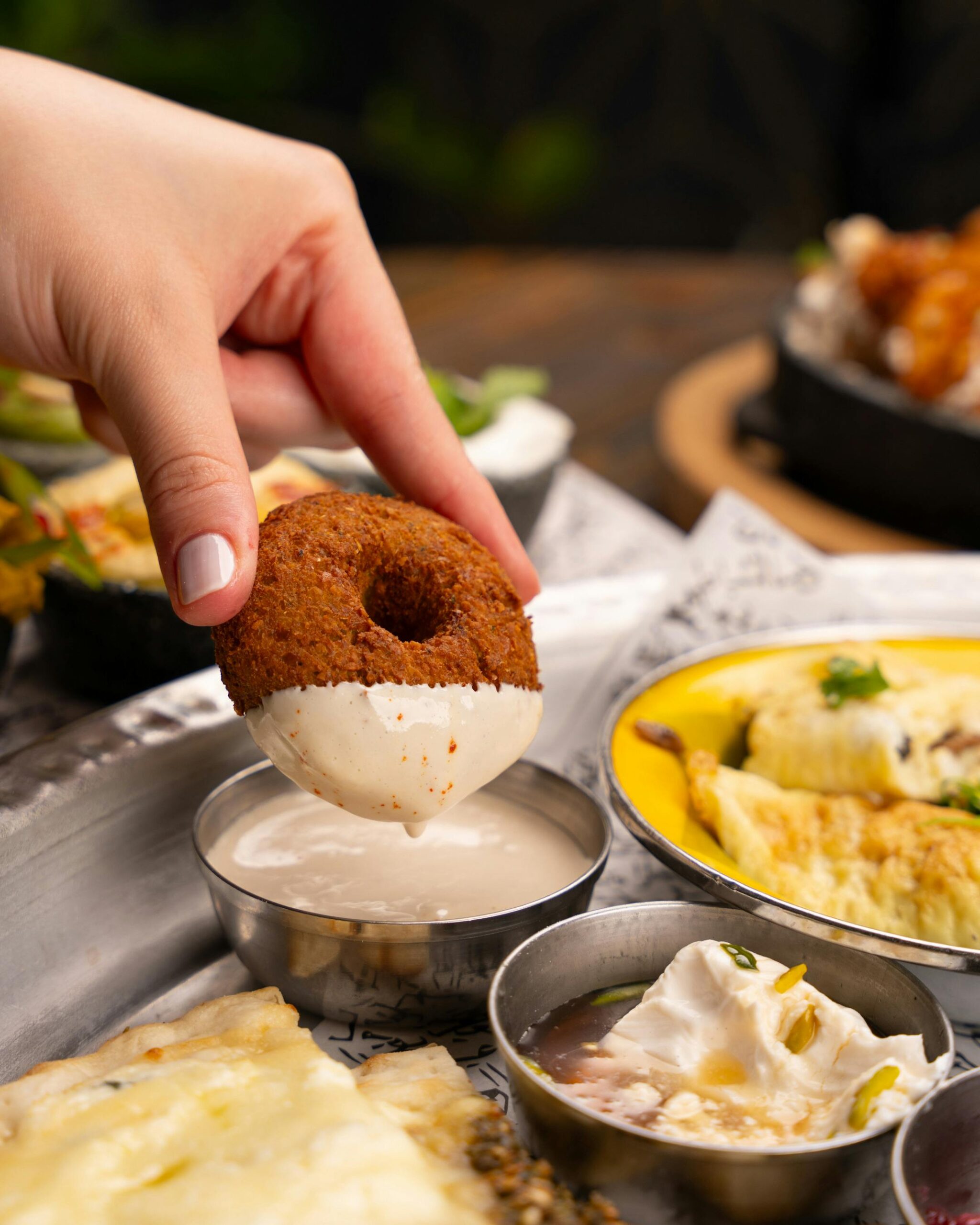 Hand dips medu vada into flavorful coconut chutney on a traditional platter.